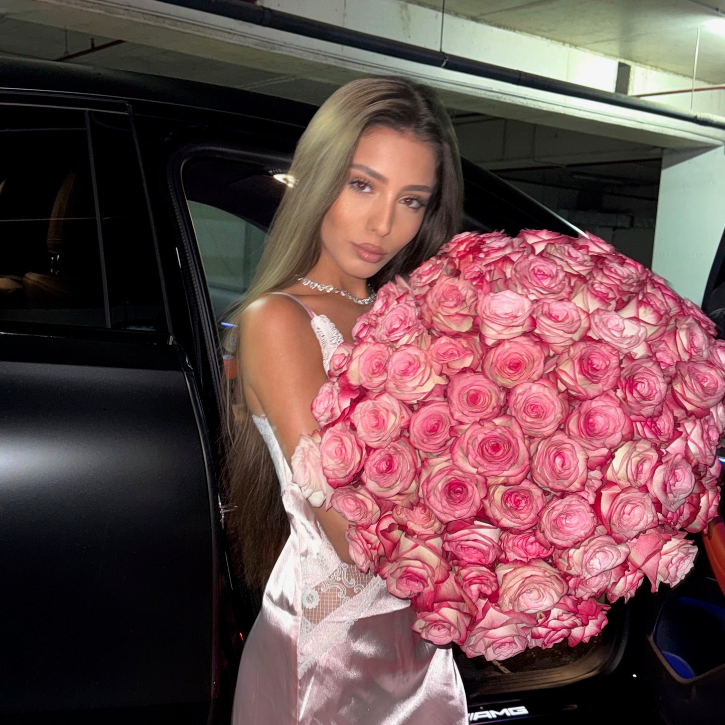 Woman holding a large bouquet of pink roses in front of a black limousine.