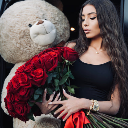 Woman holding red roses next to a large teddy bear