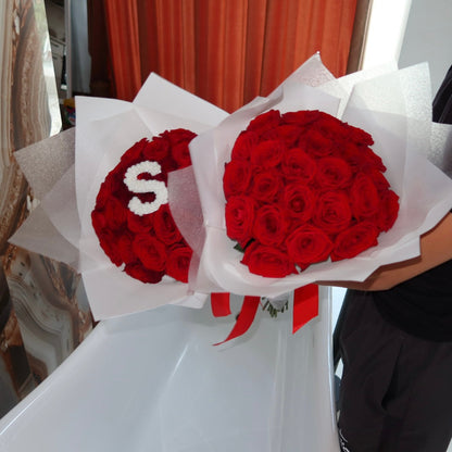 Two bouquets of red roses with a letter 'S' on a white surface.