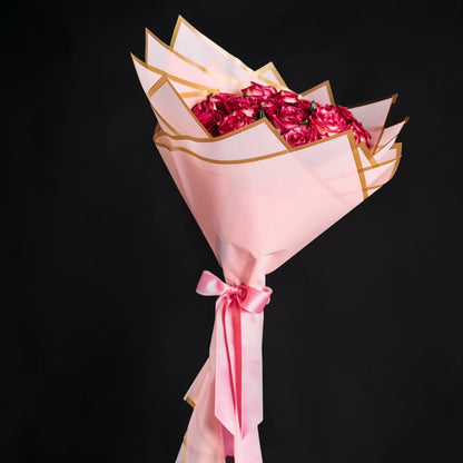 Bouquet of pink flowers wrapped in gold and pink paper with a bow on a black background