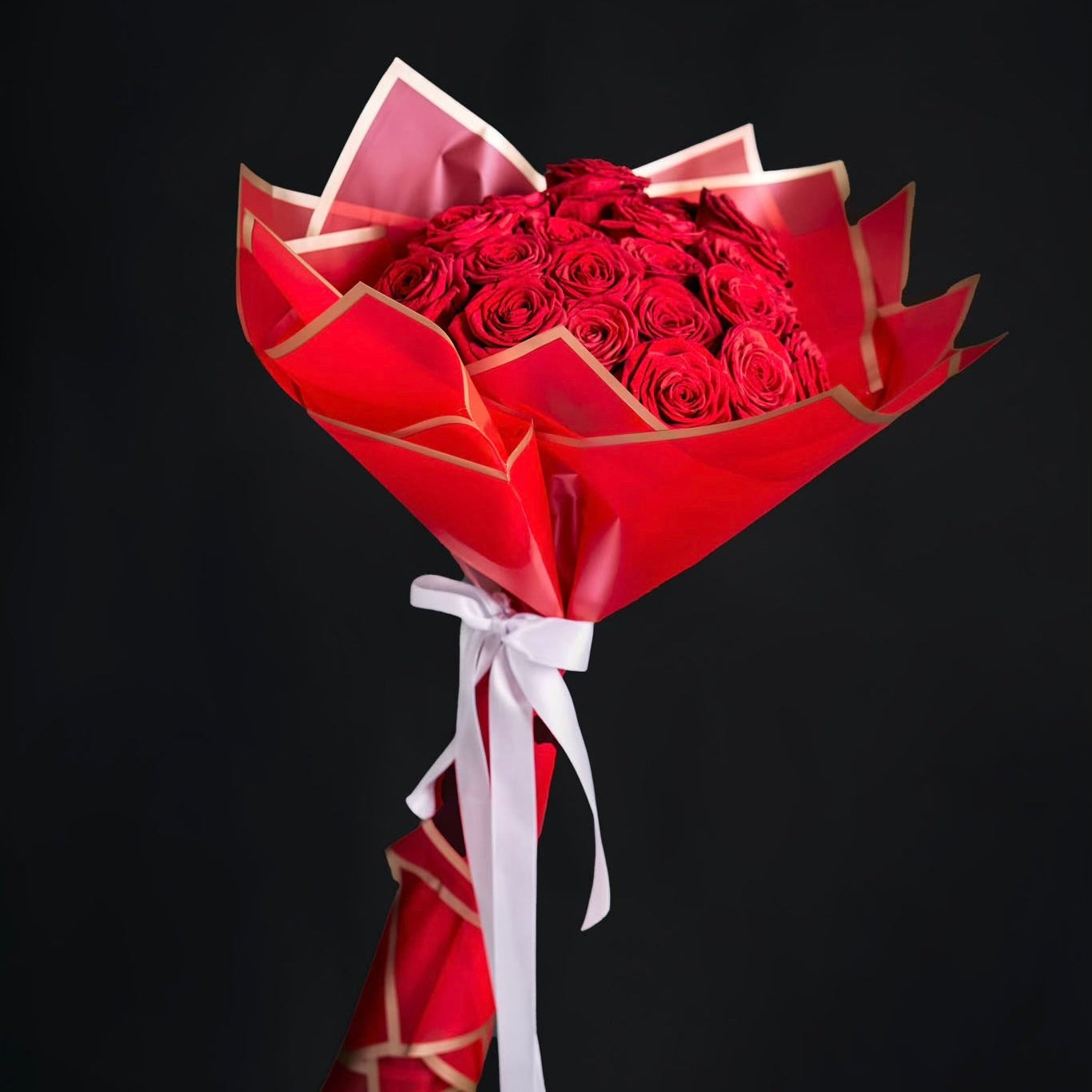 Bouquet of red roses wrapped in red paper with a white ribbon on a black background