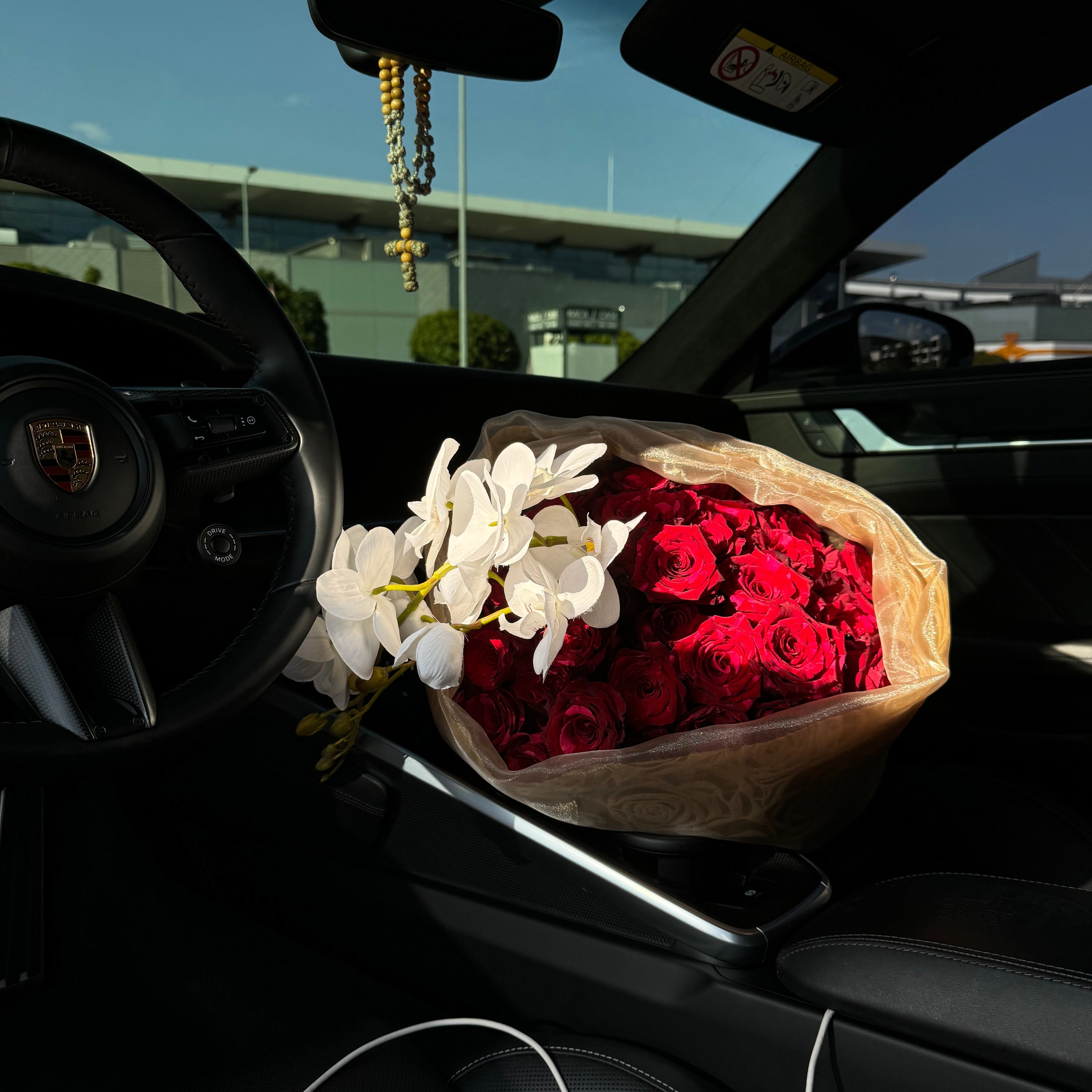 Bouquet of red roses and white flowers inside a car with a blurred cityscape background