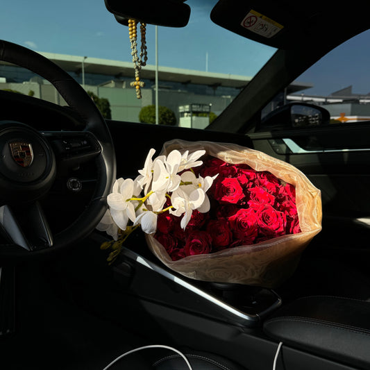 Bouquet of red roses and white flowers inside a car with a blurred cityscape background