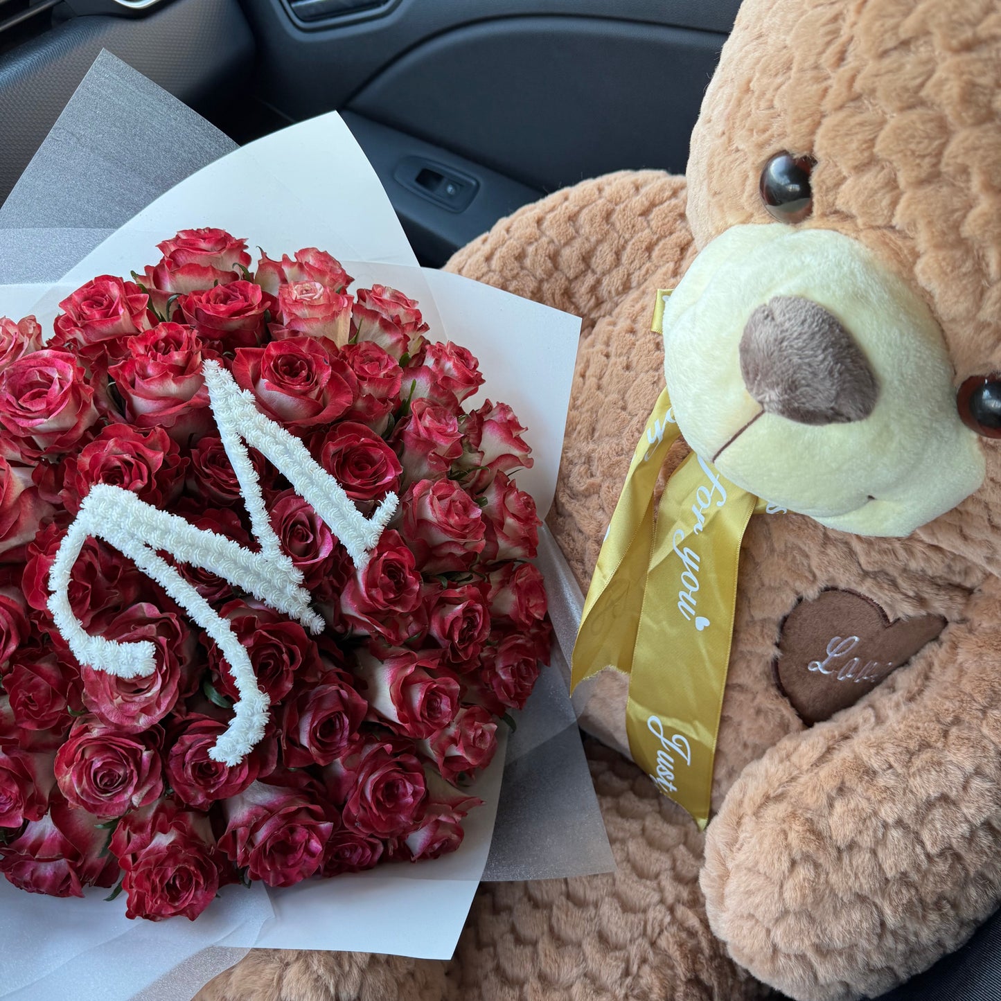 Bouquet of red roses with 'I love you' card and teddy bear in car interior