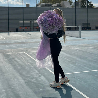 Person holding a large bouquet of purple flowers on a tennis court