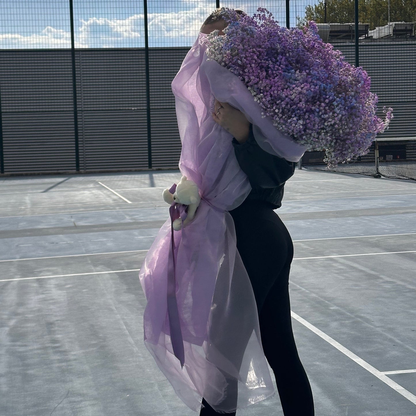 Person holding a large bouquet of purple flowers on a tennis court
