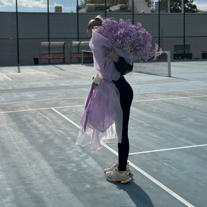 Person holding a large bouquet of purple flowers on a tennis court