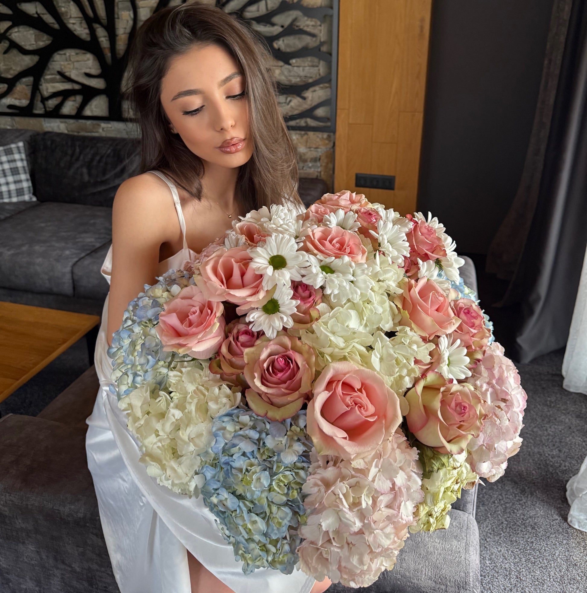 Woman holding a large bouquet of flowers in a room with a tree wall decoration.