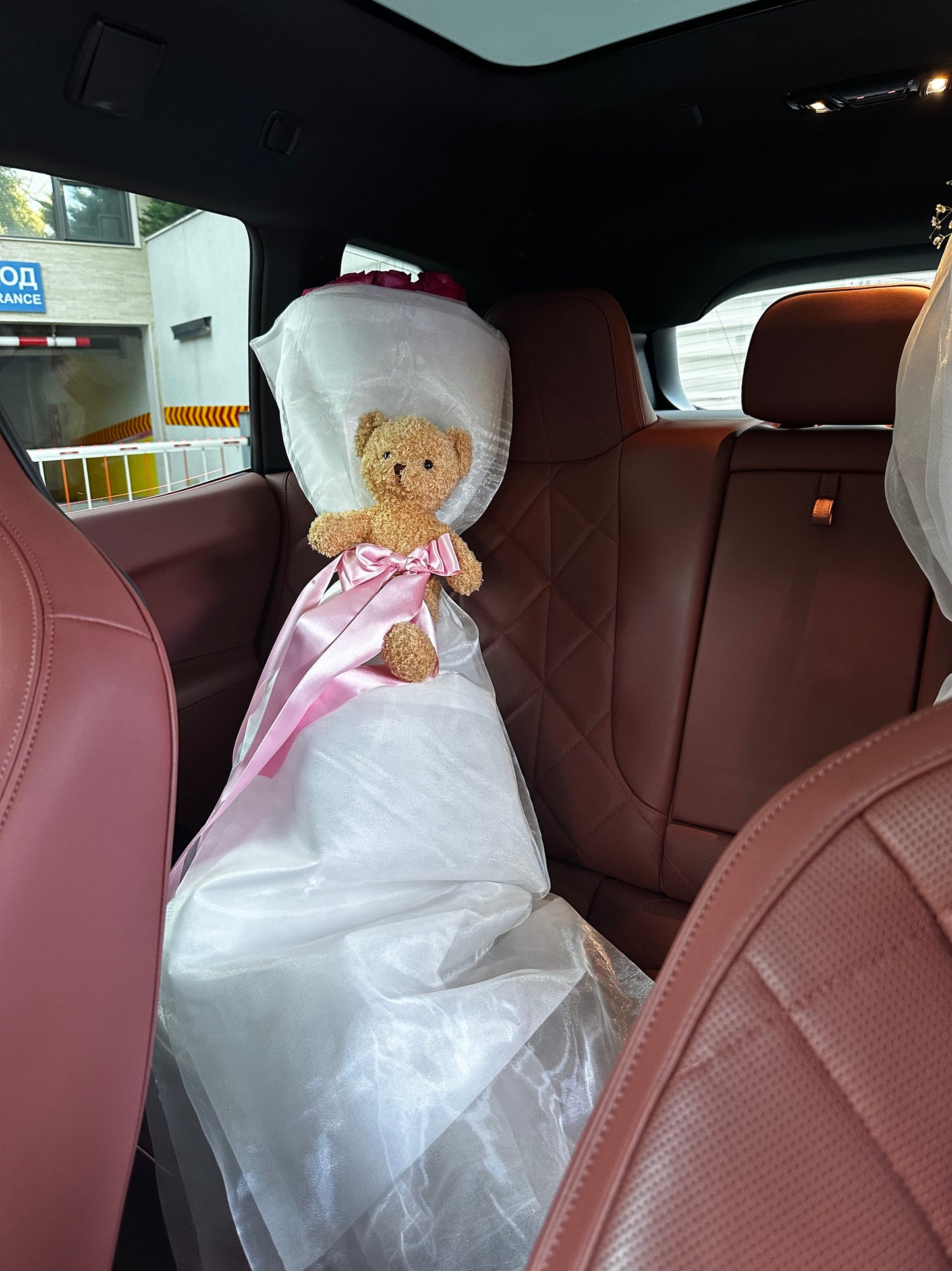 Teddy bear in a wedding dress sitting in the back seat of a car.