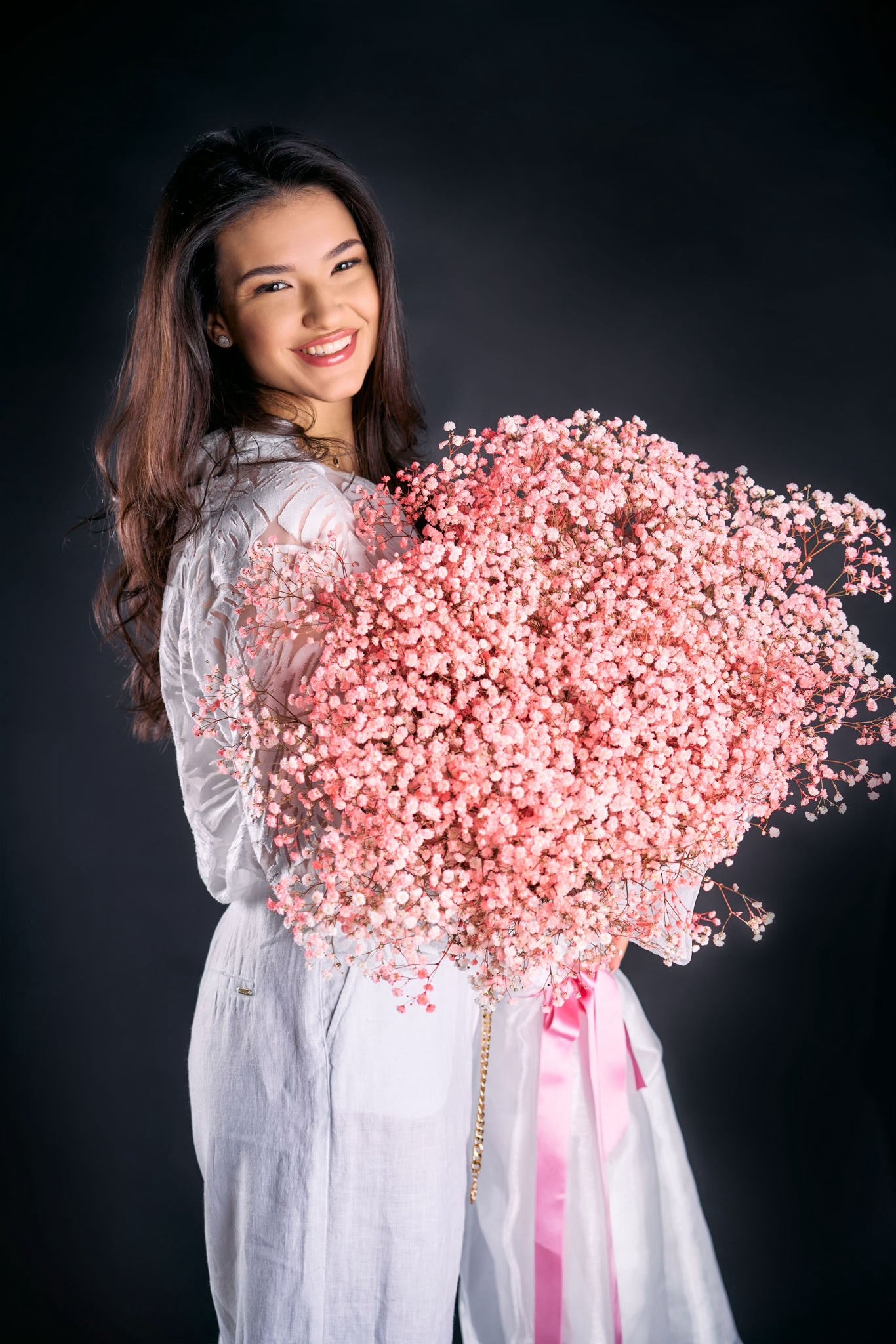 Woman holding a large bouquet of pink flowers against a black background