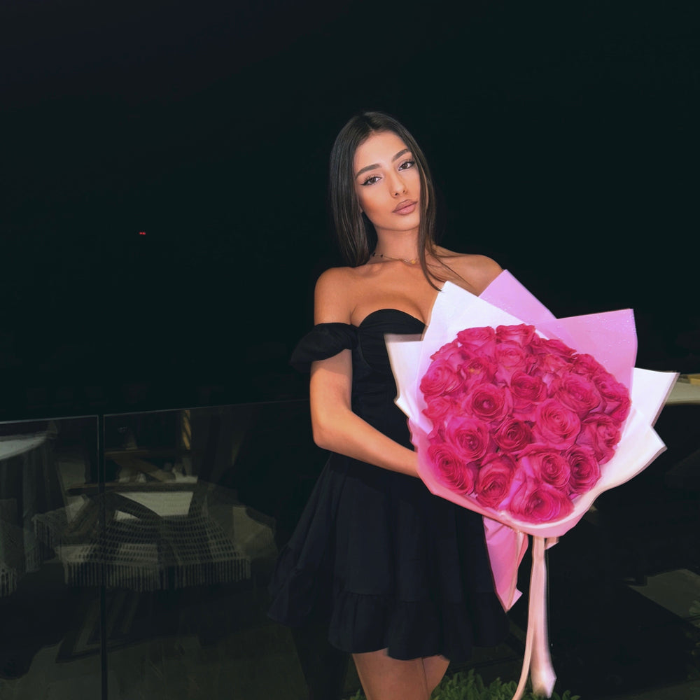Woman in a black dress holding a bouquet of pink roses against a dark background
