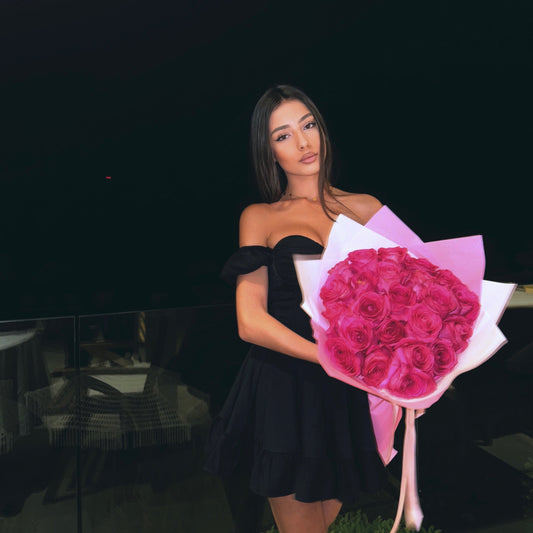 Woman in a black dress holding a bouquet of pink roses against a dark background