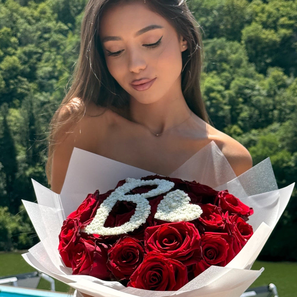 Woman holding a bouquet of red roses with 'LOVE' spelled out in white flowers against a green outdoor background