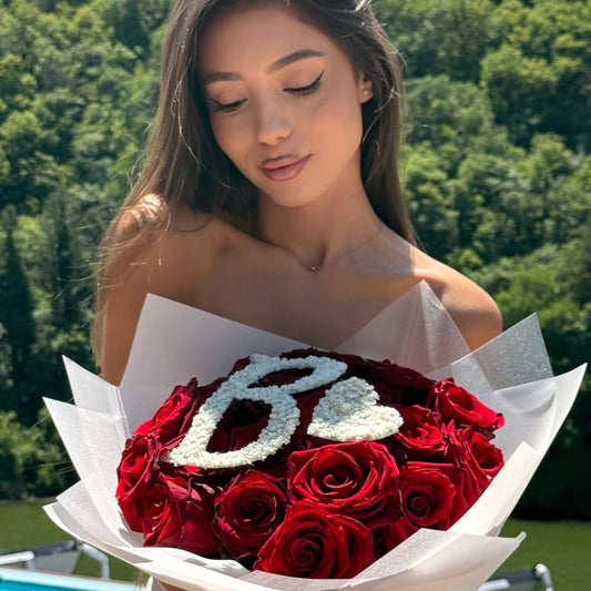 Woman holding a bouquet of red roses with 'LOVE' spelled out in white flowers against a green outdoor background