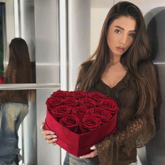 Woman holding a red heart-shaped box of roses in front of a mirror.