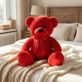 Red teddy bear with a bow tie on a bed in a bedroom setting