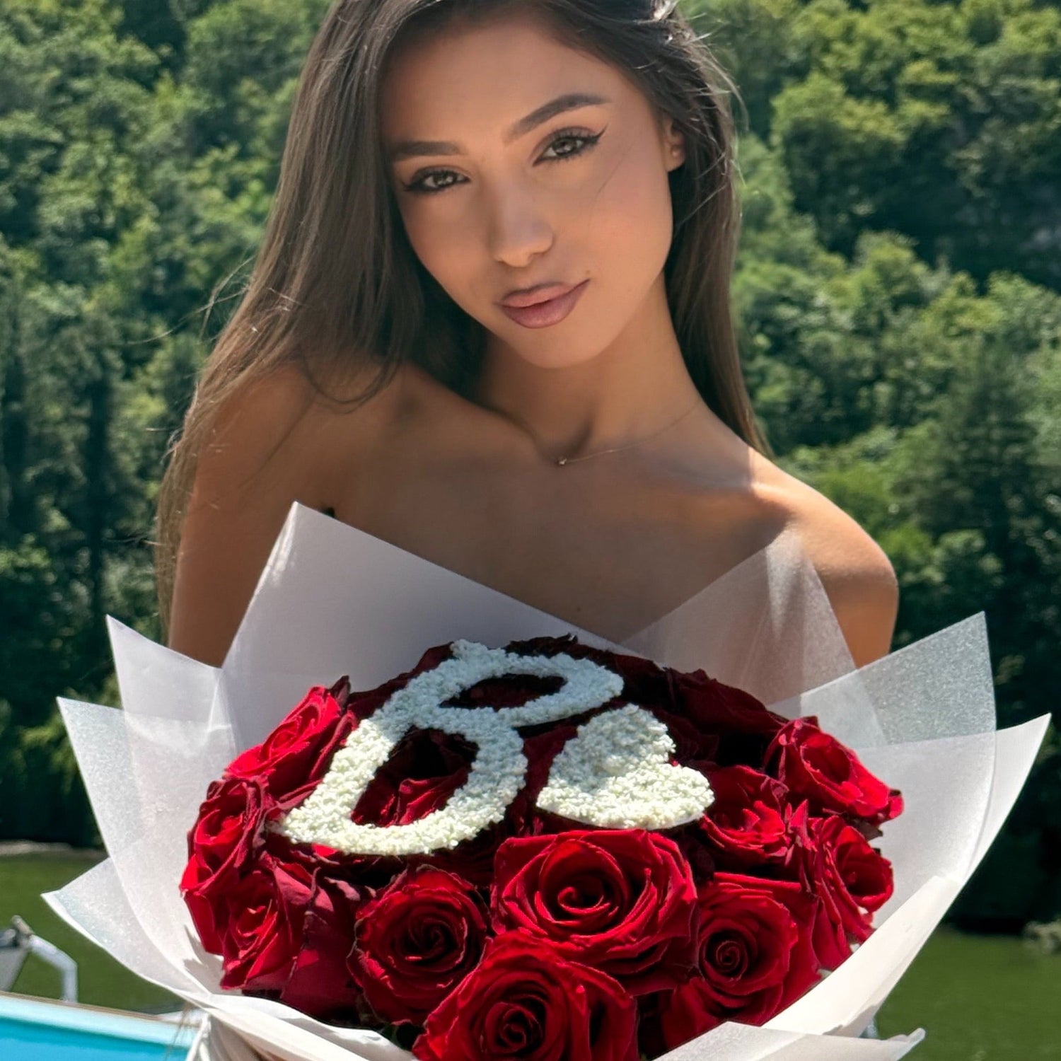 Woman holding a bouquet of red roses with 'LOVE' spelled out in white letters, outdoors.