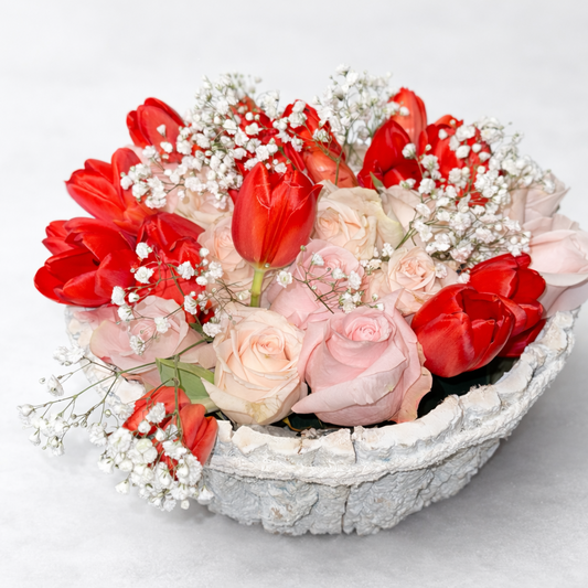 Floral arrangement with red tulips and pink roses in a decorative bowl on a white background