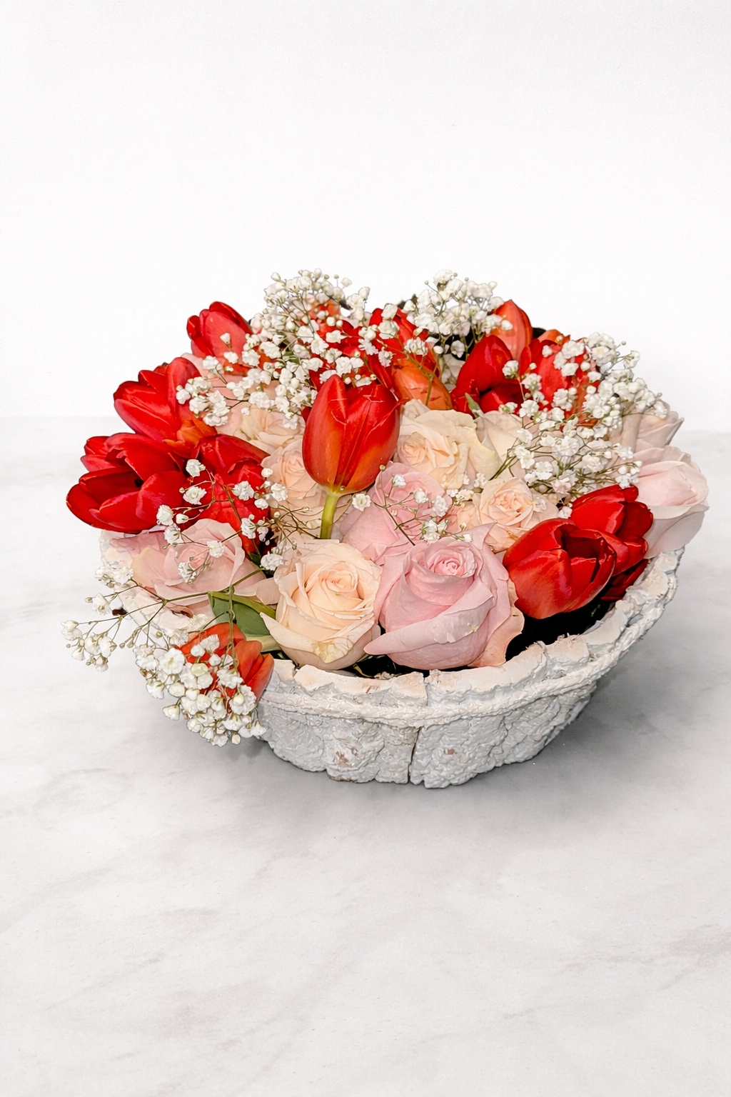 Bouquet of red and pink flowers in a decorative stone bowl on a white background