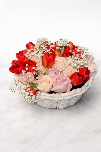 Bouquet of red and pink flowers in a decorative stone bowl on a white background